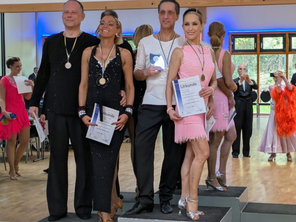 Es stehen zwei Paare auf dem Siegerpodest. Flavio und Nadine stehen auf dem 1. Platz und halten die Siegerurkunde in der Hand.