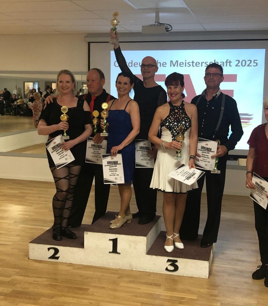 Drei Paare stehen auf dem Siegerpodest. Roland hält den pokal in die Höhe.