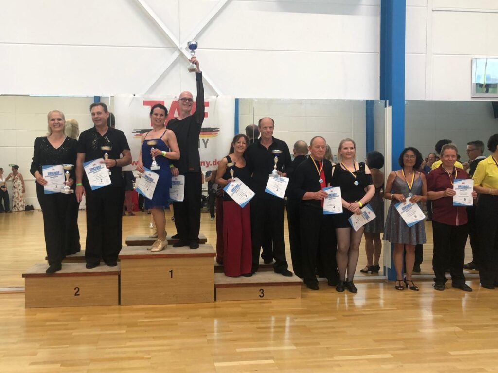 Siegerehrung mit 6 Paaren. Roland und Renate stehen auf dem ersten Platz und halten den Pokal in die Höhe